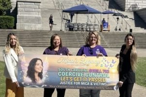 Four women hold a 'Mica's Legacy — SC Bill 702, Coercive Control' banner on the South Carolina State House steps
